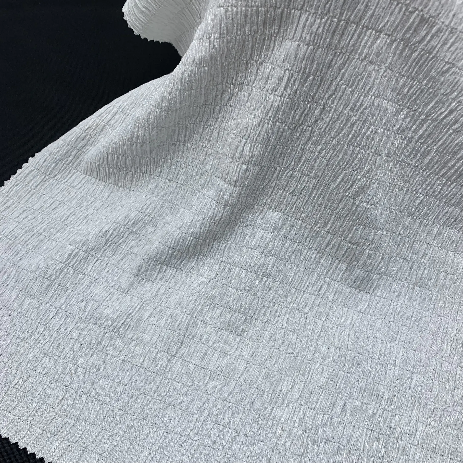 Close up of white stretch crepe knit fabric showing 4-way stretch and textured surface